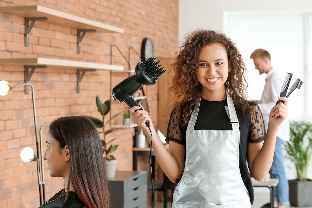 Young African-American hairdresser in beauty salon holding tools that are tax deductions for hairdressers in Australia